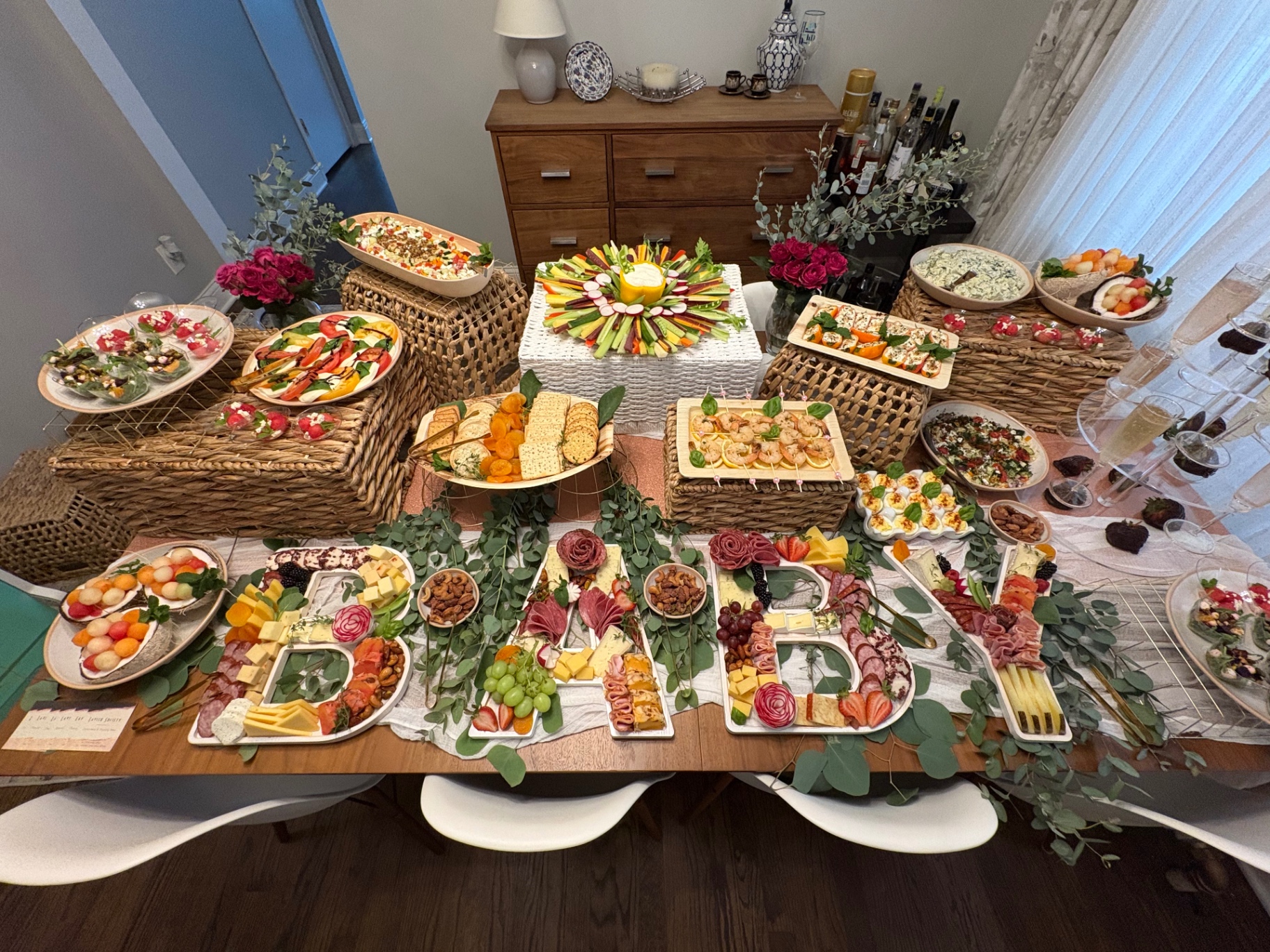 Baby shower table with charcuterie letter trays spelling BABY, a crudite wreath, and appetizers